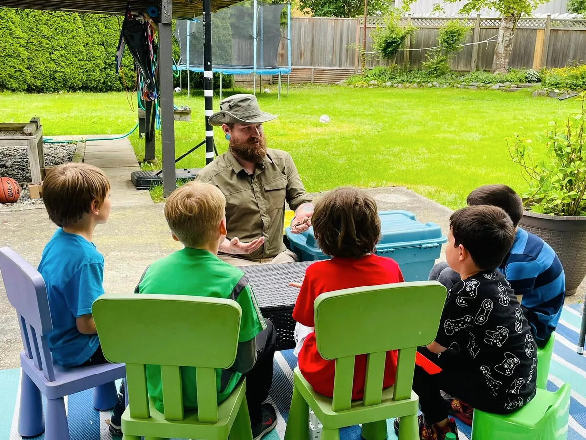 Kevin presenting an animal to a seated group of children during an educational visit.